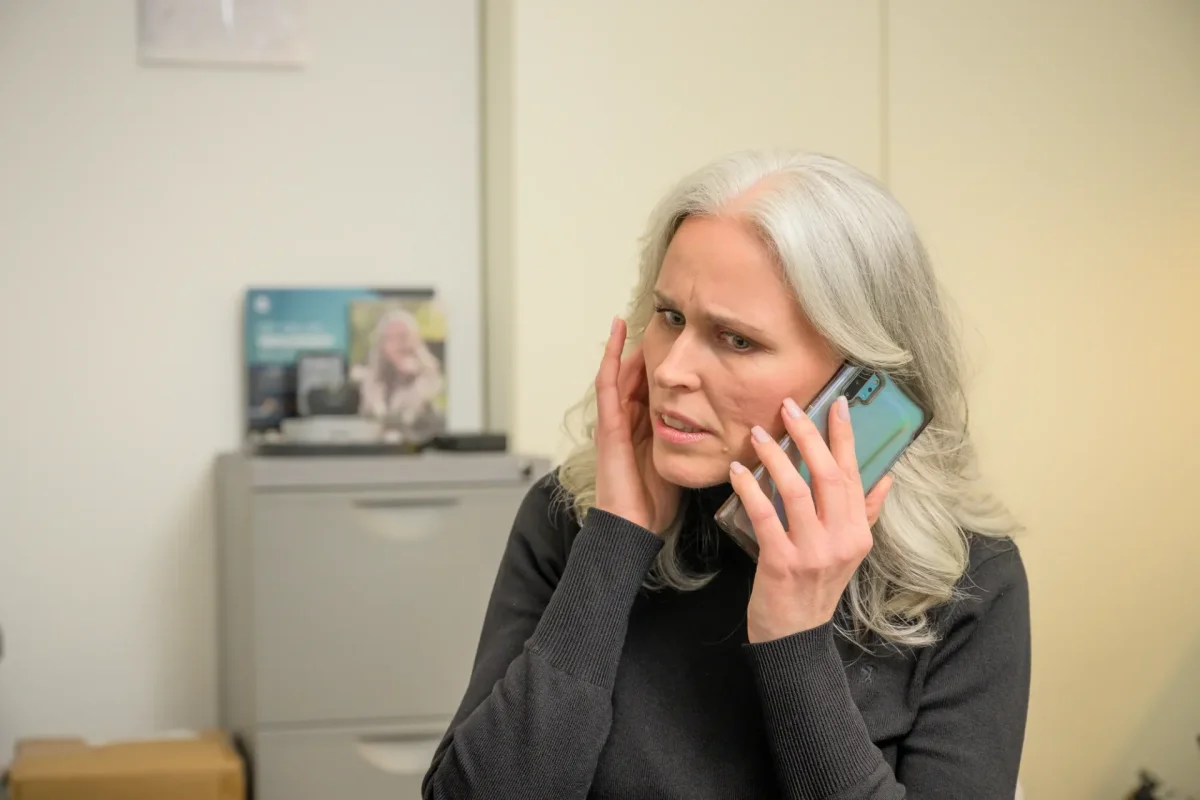 Vrouw aan de telefoon houdt haar hand bij haar oor omdat ze de ander slecht verstaat