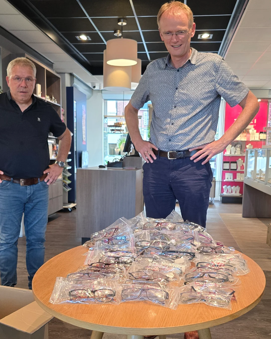 Opticien Cris (links) en huisarts Arntzen (rechts) bij de tafel met de 300 brillen voor Zambia in de winkel van Von Oy